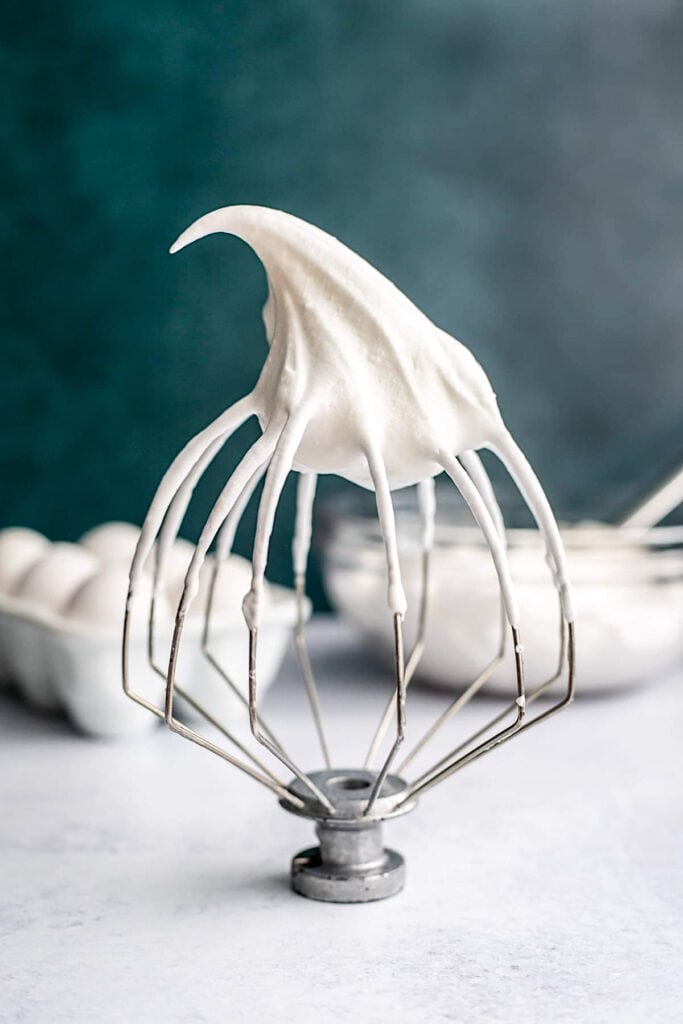Whisk attachment with Italian meringue in front of eggs and a bowl of meringue