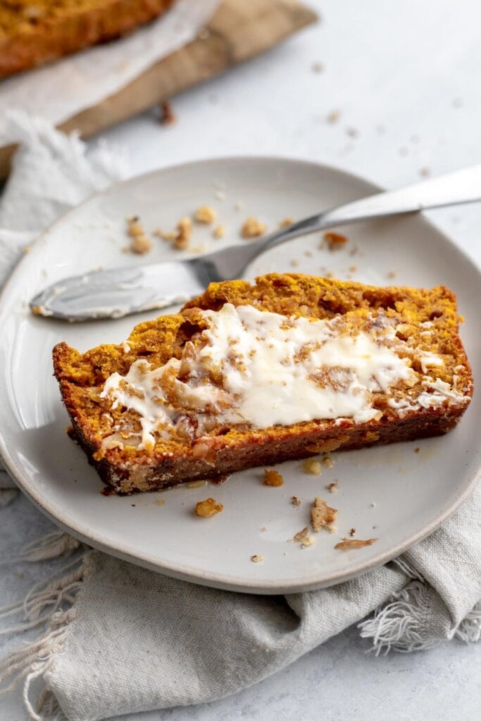Slice of pumpkin banana bread slathered with butter on a plate
