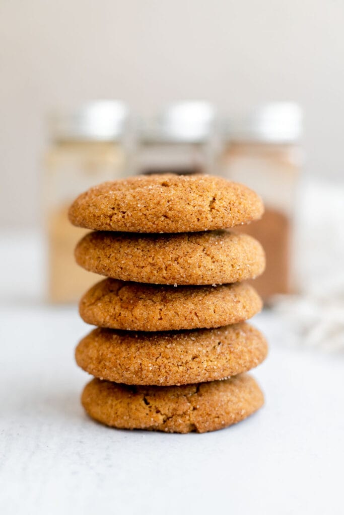 Stack of vegan gingerdoodles in front of jars of cinnamon, cloves, and ginger