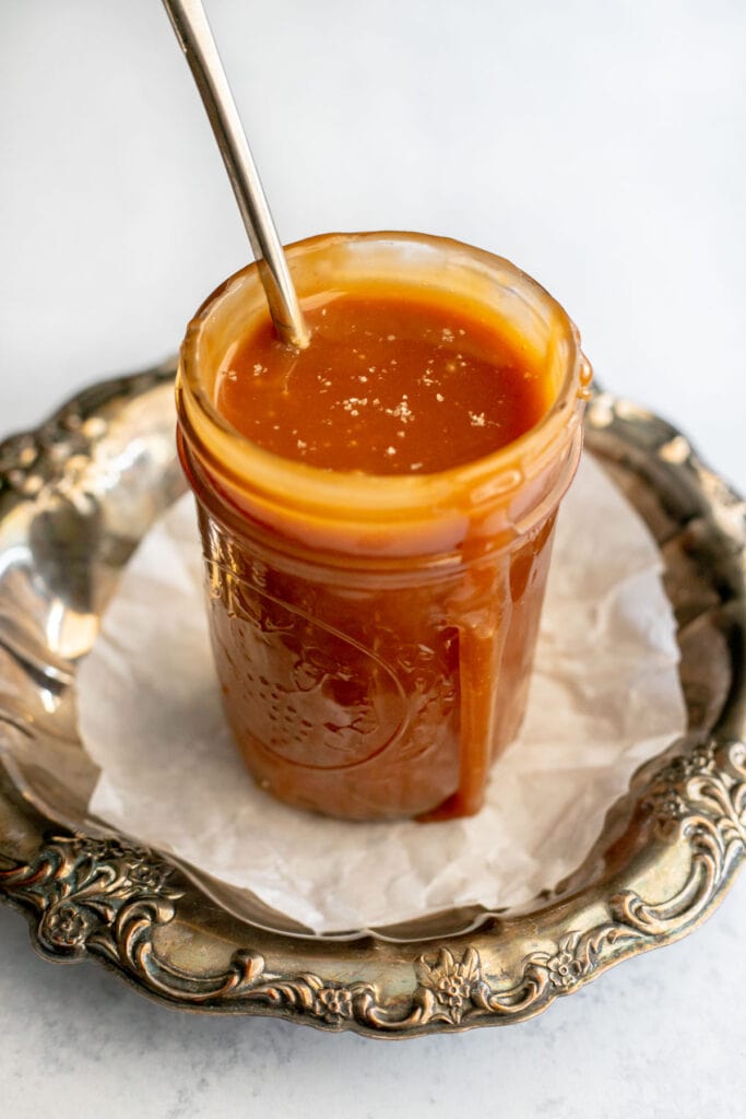Jar of caramel sauce with a spoon resting in it on top of a bronze serving platter