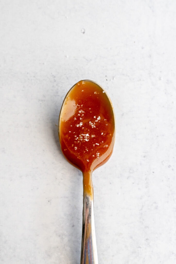Spoon of caramel sauce resting on a grey surface