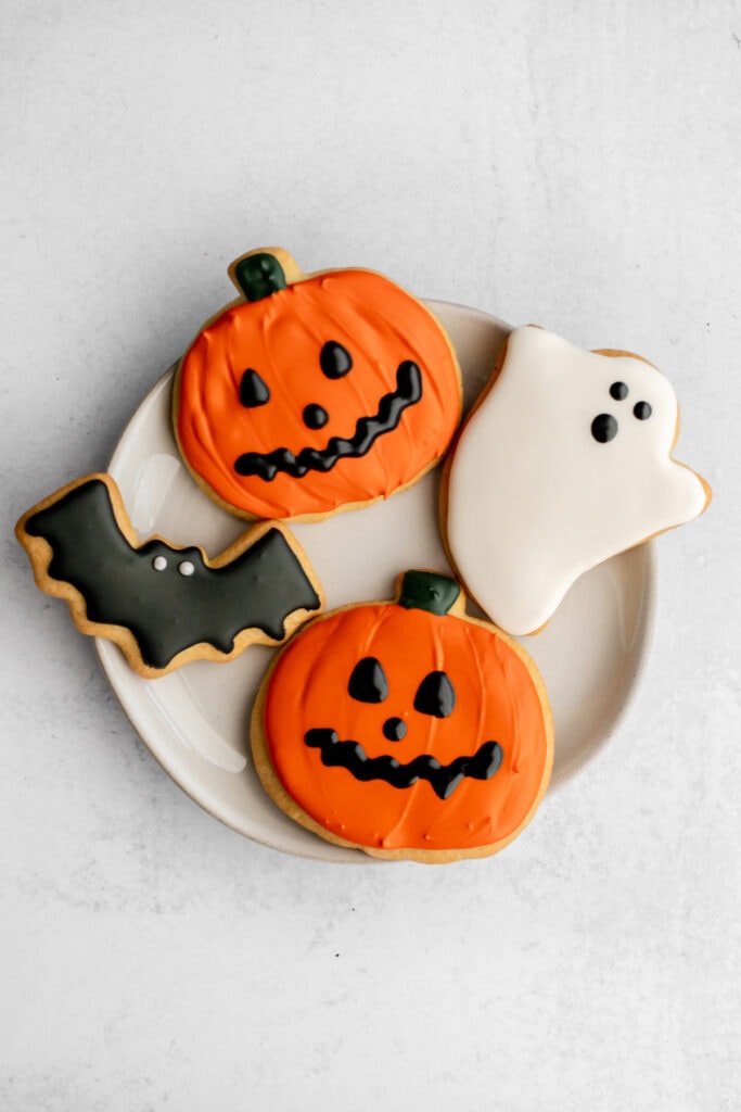 A plate of pumpkin, bat, and ghost sugar cookies decorated with royal icing