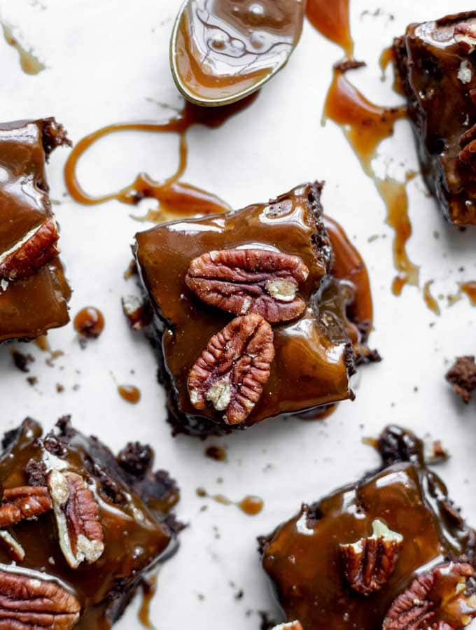 Salted caramel turtle brownies resting around a spoon of caramel