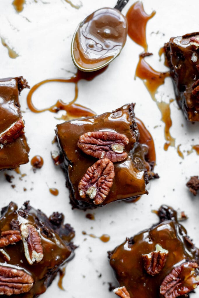 Several salted caramel turtle brownies resting next to a spoon of caramel