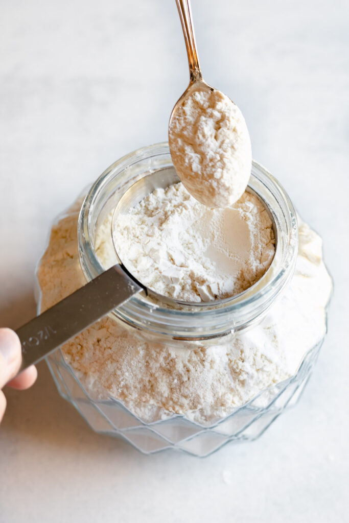 Hand scooping flour into a metal measuring spoon