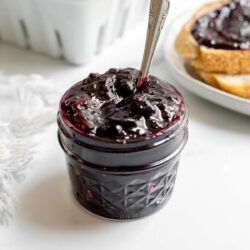 Jar of cherry berry jam in front of a stack of toast