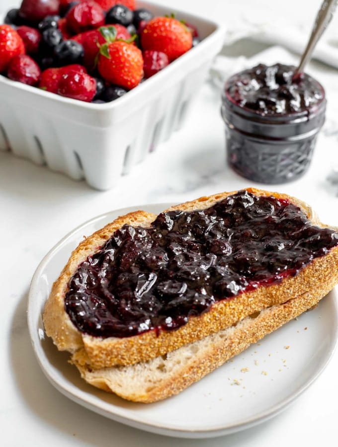 Cherry berry jam on top of two bread slices in front of a jar of jam and a basket of fruit