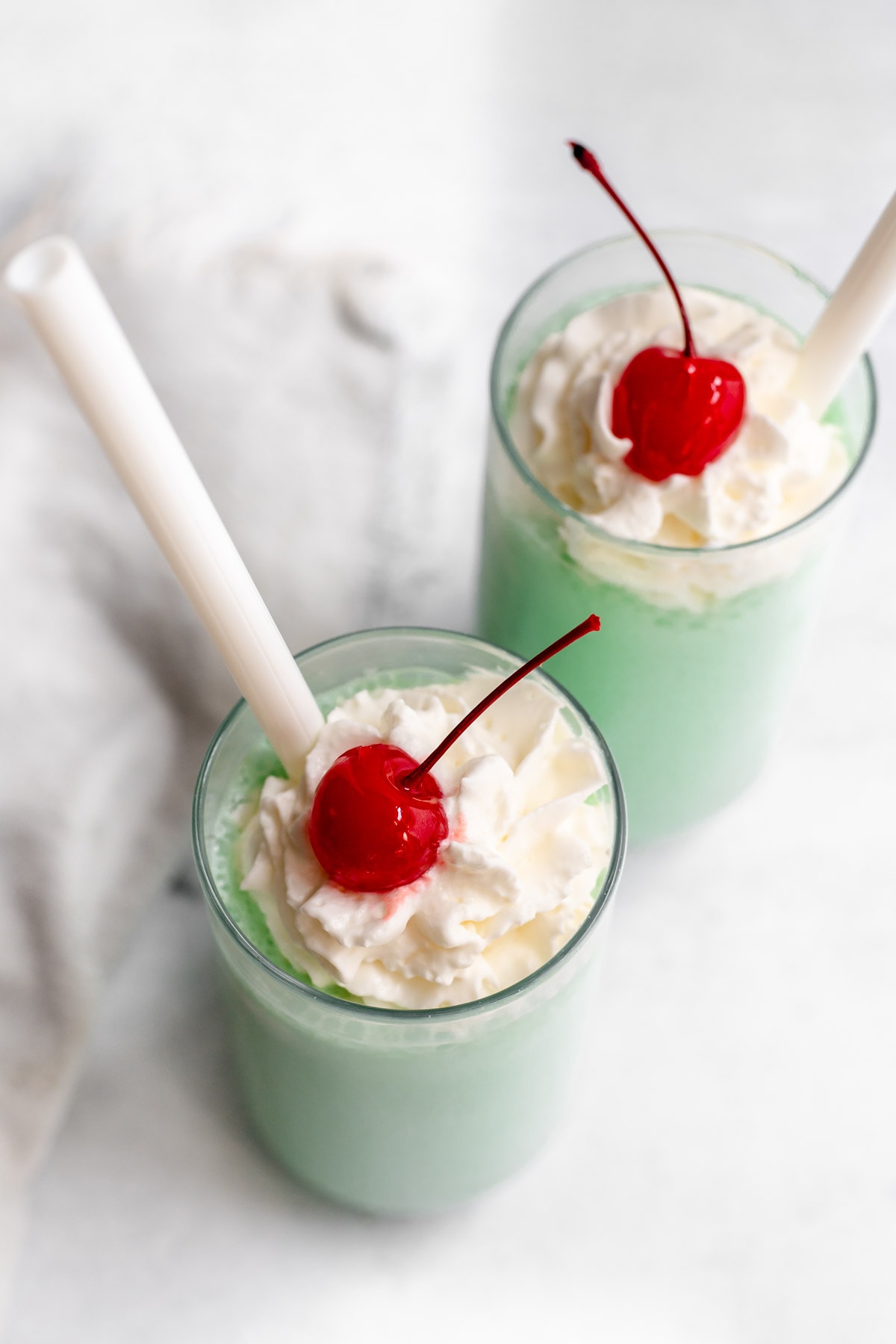Two shamrock shakes in glasses topped with whipped cream and maraschino cherries