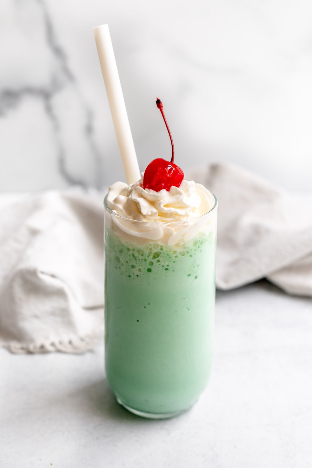 Glass with green shamrock shake topped with whipped cream, a cherry, and a straw
