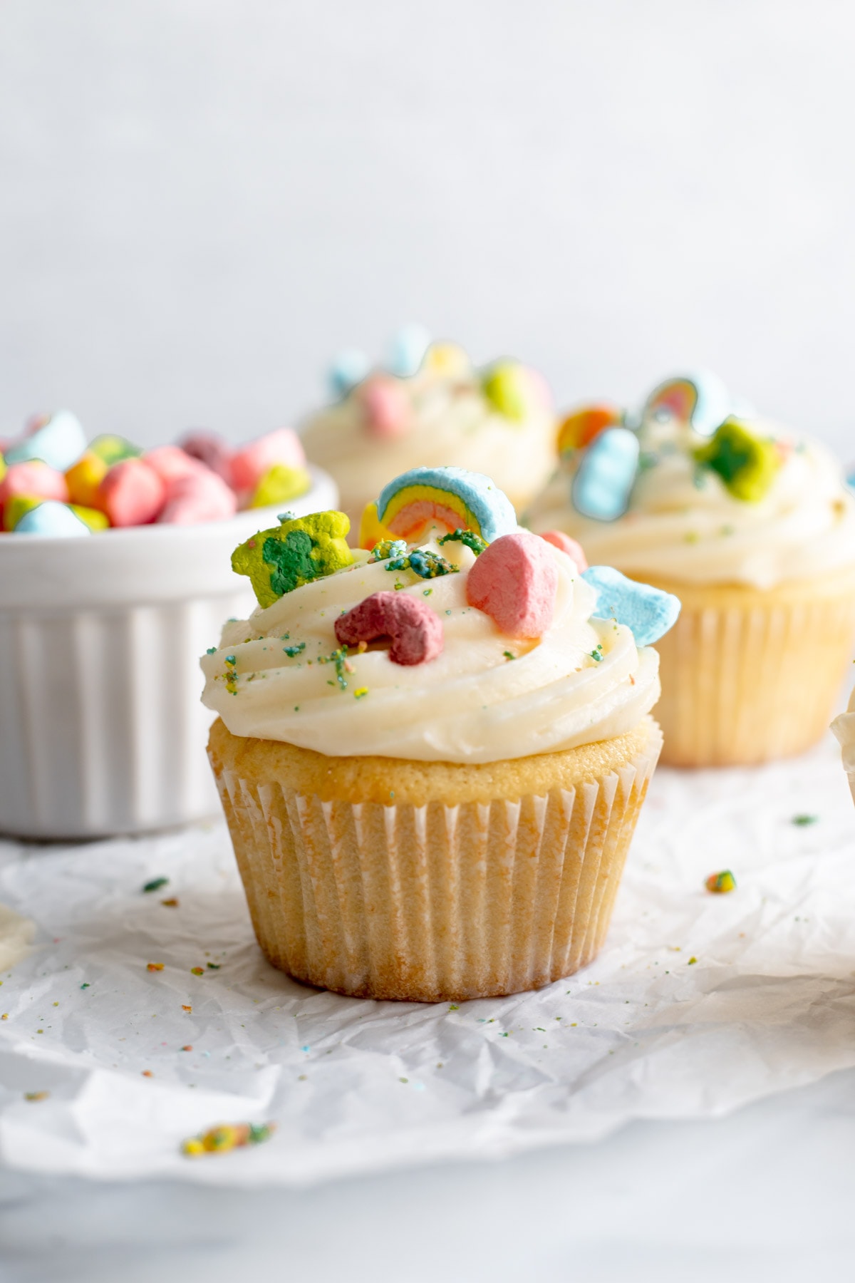 Three cupcakes topped with cream cheese frosting and Lucky Charms cereal 