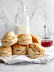 Stack of buttermilk biscuits in front of a jar of milk and a jar of strawberry jam