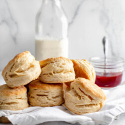 Stack of buttermilk biscuits in front of a jar of milk and a jar of strawberry jam