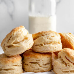 Stack of buttermilk biscuits in front of a jar of milk and a jar of strawberry jam with text that reads 'Buttermilk Biscuits'