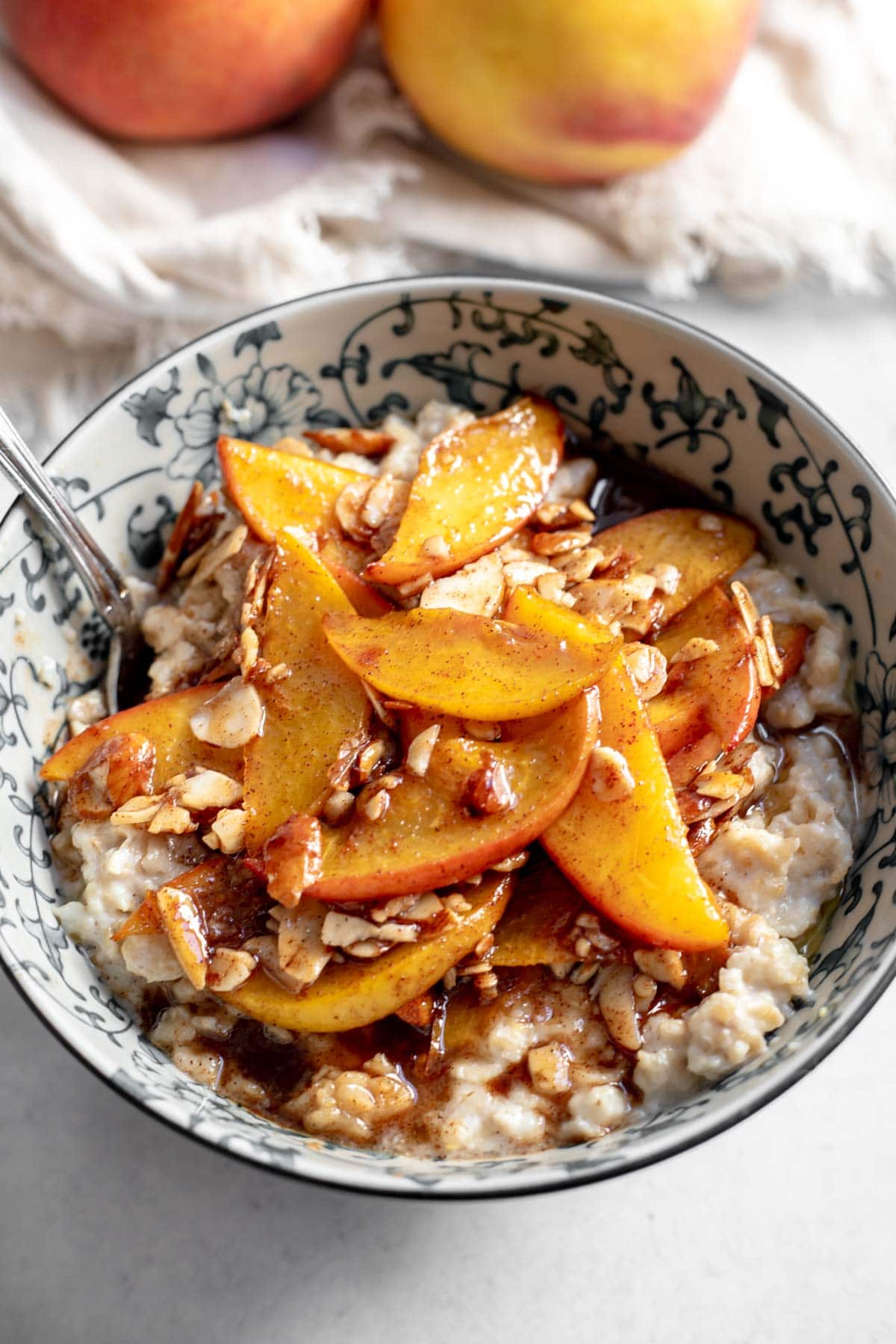 Bowl of oatmeal topped with peaches and almonds in front of two peaches