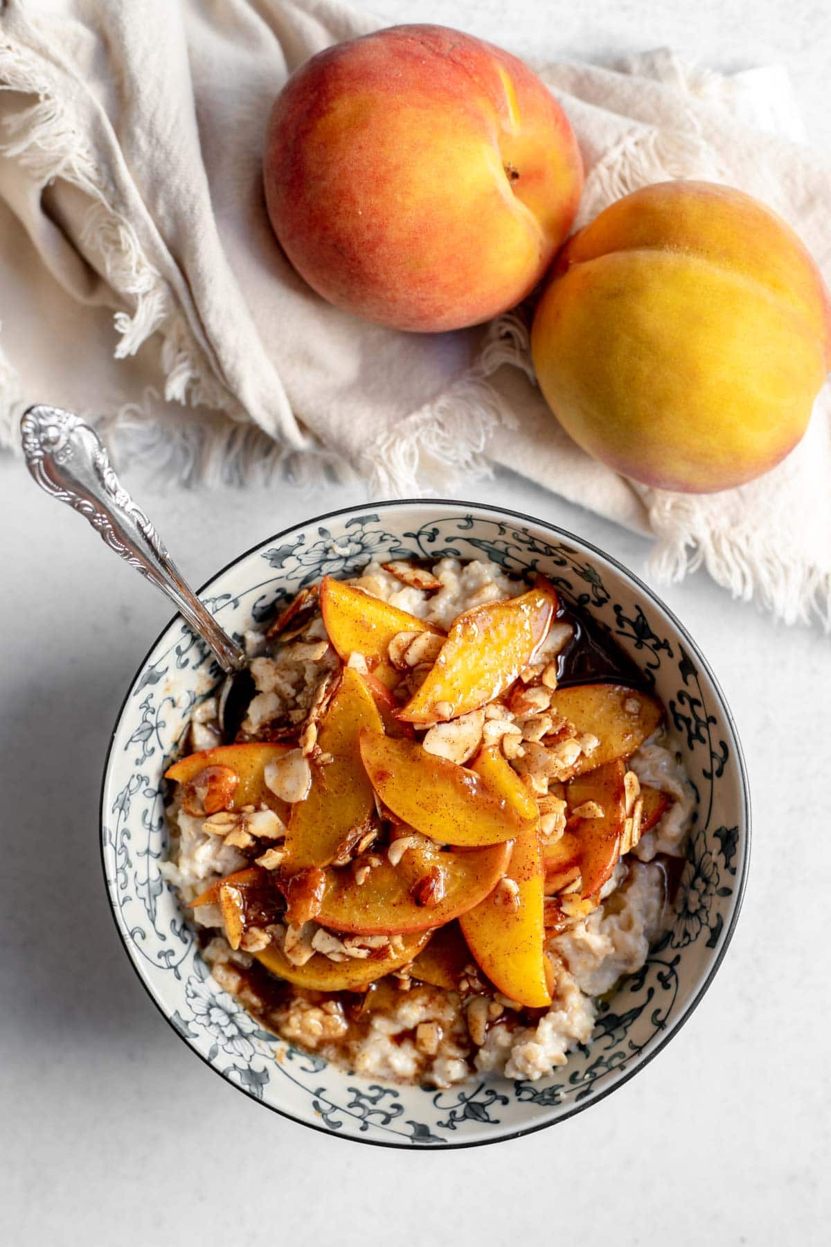 Bowl of oatmeal topped with peaches and almonds in front of a napkin and two peaches