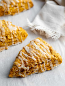 Three pumpkin scones on parchment paper in front of a napkin