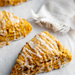 Three pumpkin scones on parchment paper in front of a napkin