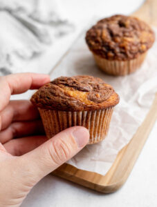 Hand holding a muffin on top of a cutting board lined with parchment paper