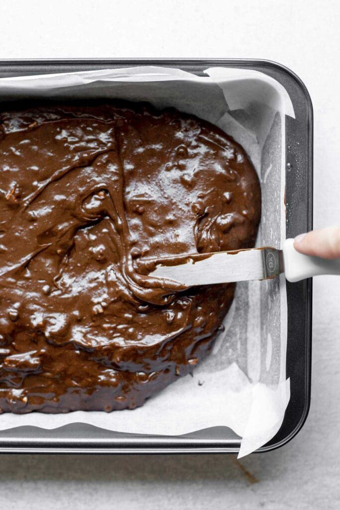 Spatula spreading brownie batter into a baking pan