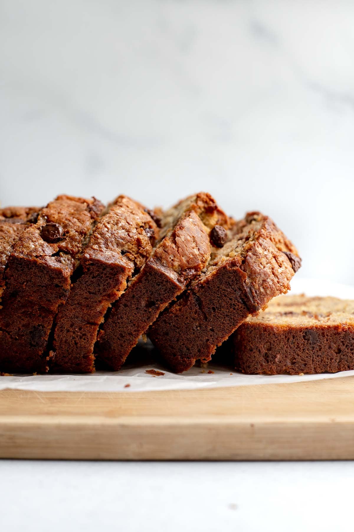 Slices of banana bread leaning over on a cutting board lined with parchment paper